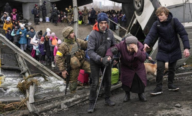 Una anciana es ayudada a cruzar el río Irpin, Ucrania, luego que las tropas rusas destruyeran un puente. AP